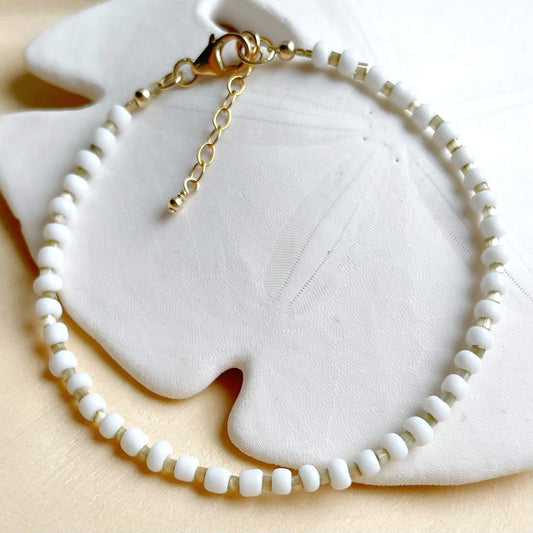 beaded white and beige bracelet with a gold clasp and ender chain.