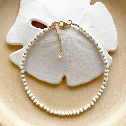 white and beige beaded anklet with gold clasp and extension chain against a sand dollar