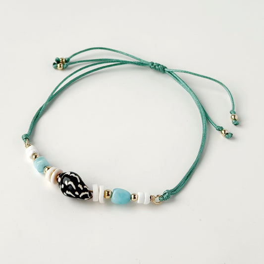 nylon teal cord bracelet with shell and gold beads on white background and tail ends