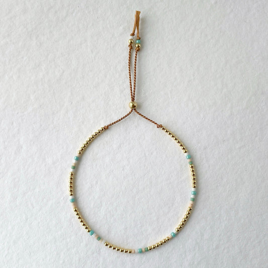 Beige silk bracelet with aqua, blush and white glass beads and 14k gold fill accents on a white background