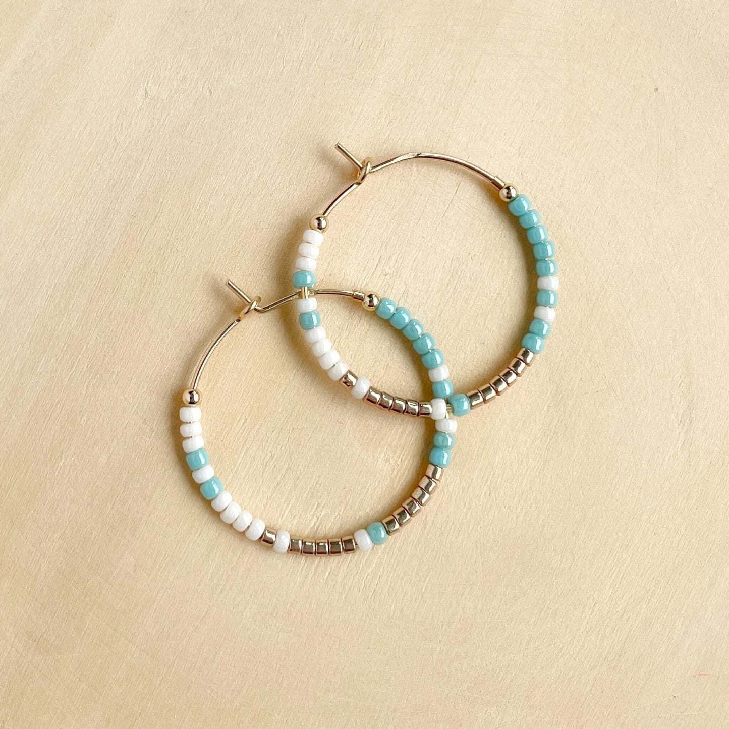 Lightweight small hoop earrings with aqua, gold and linen glass beads on gold fill hoops displayed against wood