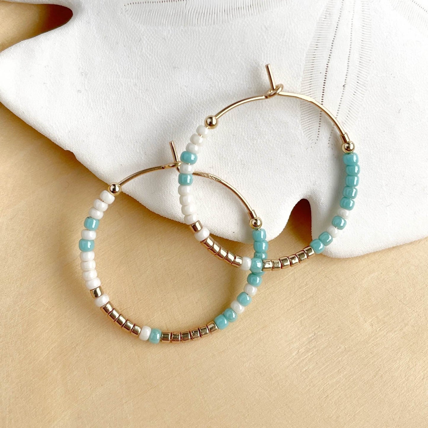 colourful hoop earrings with aqua, gold and linen glass beads on gold fill hoops displayed against a white sand dollar