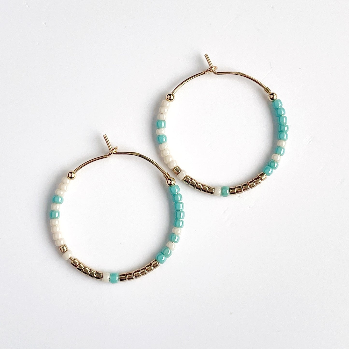 Pair of beaded gold filled hoop earrings with turquoise, gold and cream beads on a white background