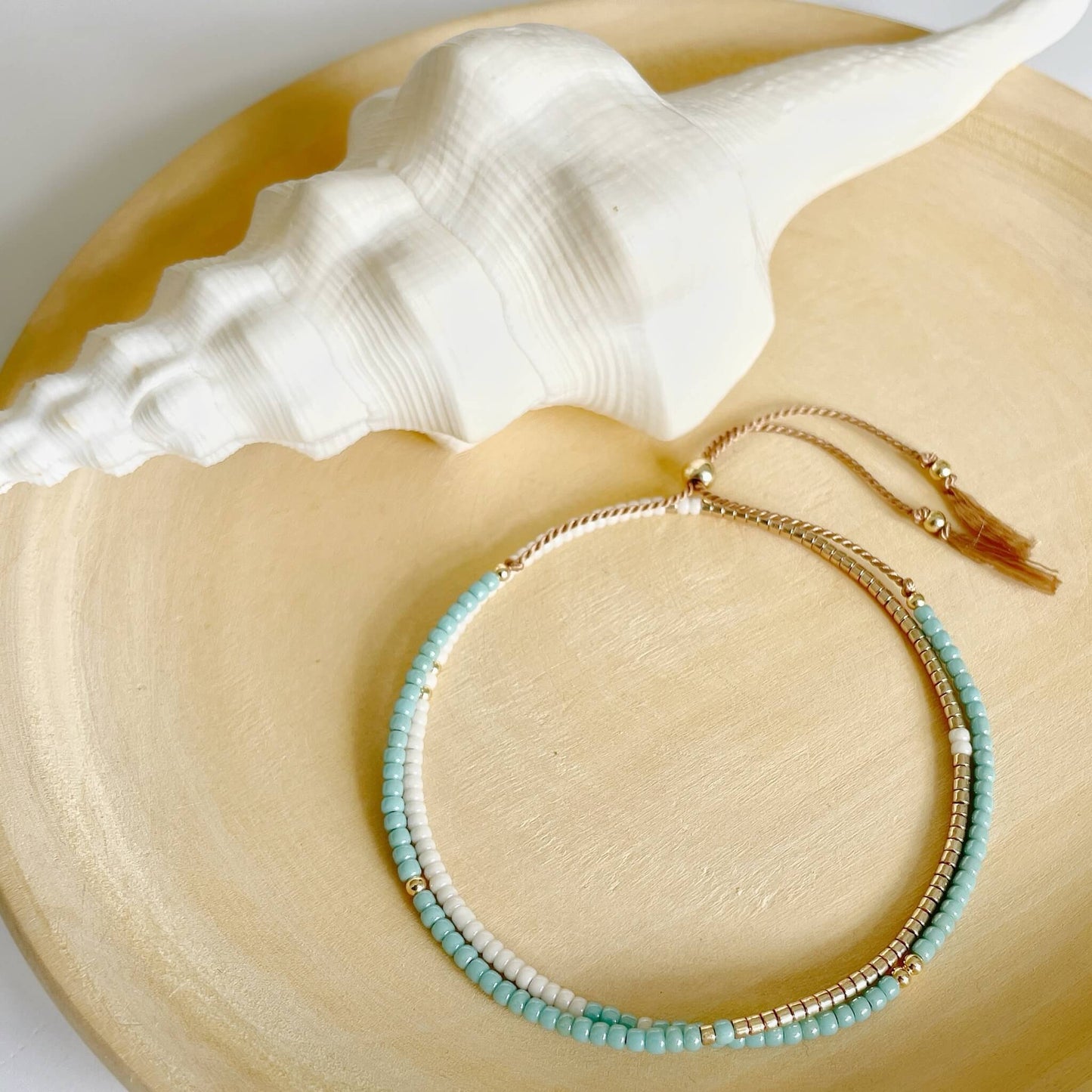 Aqua, gold and cream bracelet on a large shell with a white background