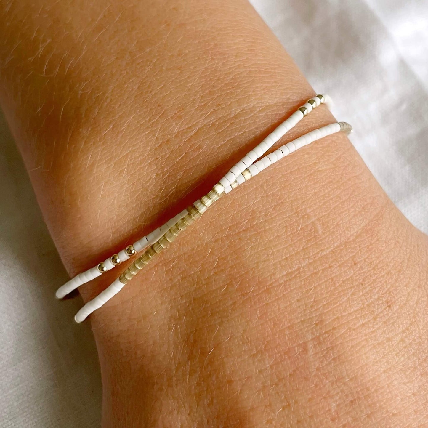 Bali-inspired double wrap bracelet worn on wrist, featuring taupe and off-white glass beads with mother of pearl and 14k gold fill accents