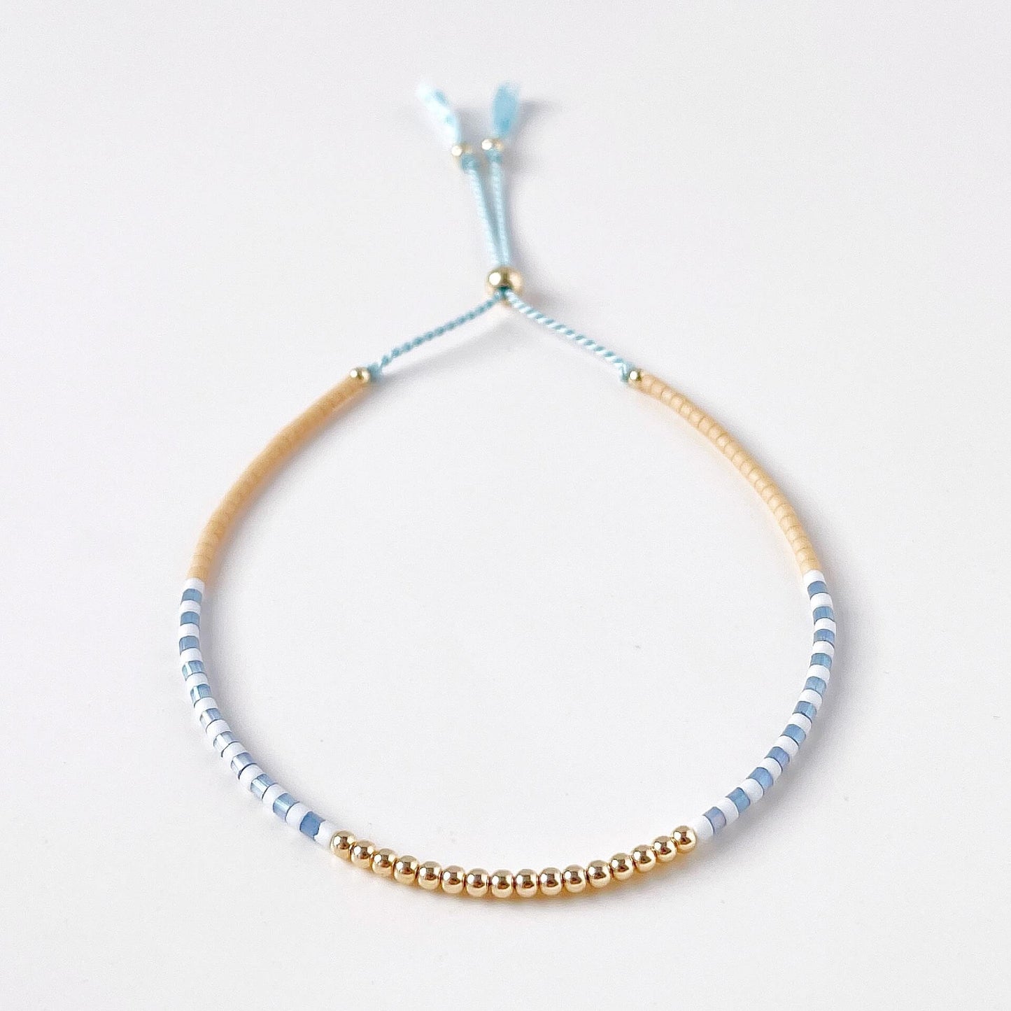 glass bead bracelet with beige, blue and white beads and 14k gold filled accents on silk cord against a white background