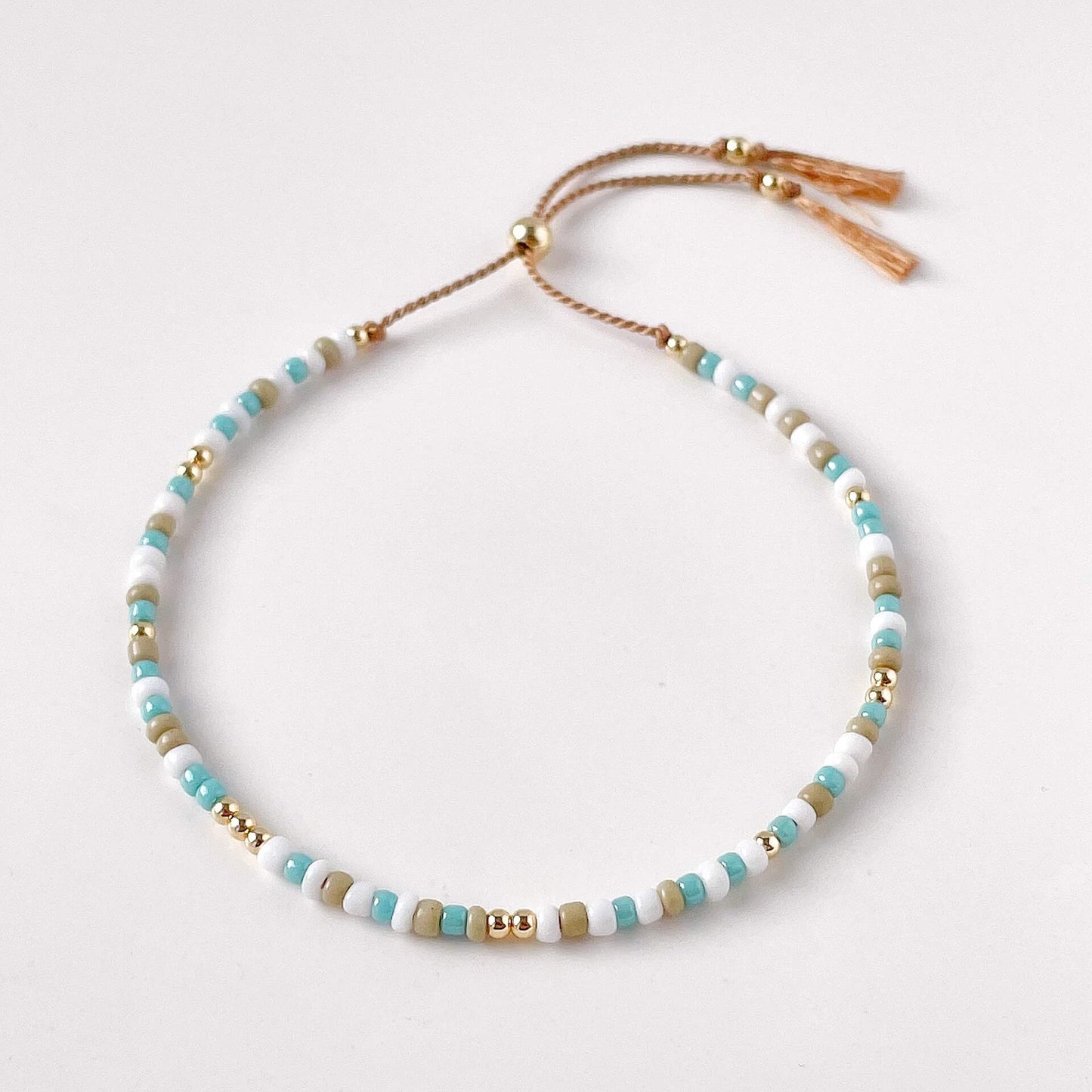 Beaded necklace with gold, turquoise, and beige beads on a light background