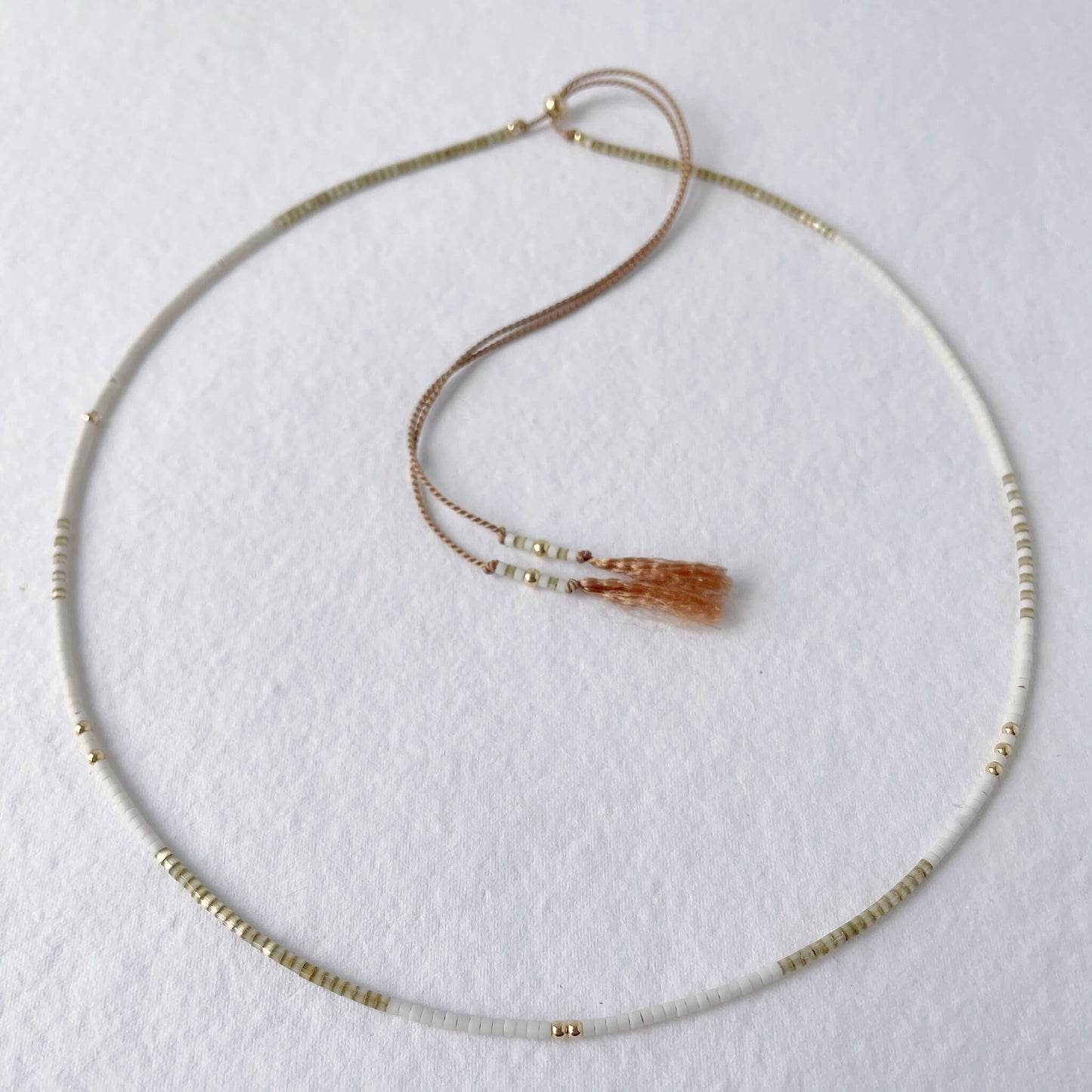 taupe and white dainty beaded necklace on a beige silk cord with tassel ends and gold adjustable sliding bead