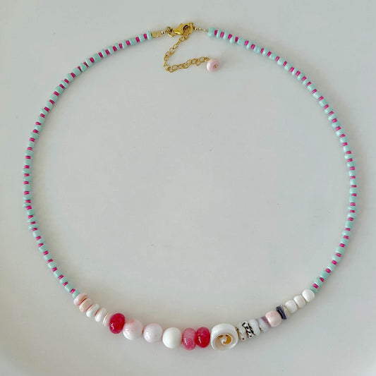 Aqua, pink, red and purple glass and shell bead necklace with gold fill clasp on a white surface