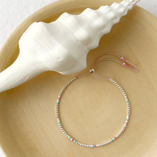Sterling silver and glass bead bracelet in reef colours pink, turquoise, lemon, mint and white displayed on a wooden plate with a large white shell
