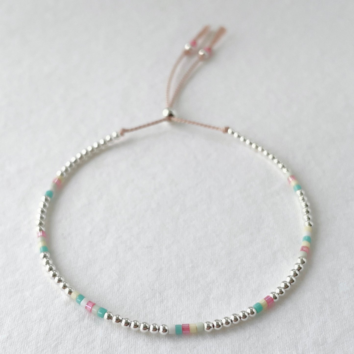 Beaded bracelet with silver, turquoise, and pink beads on a white background