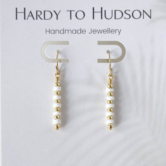 Pair of earrings with white shell and gold fill with French ear hooks beads on a white background, branded as Hardy to Hudson.
