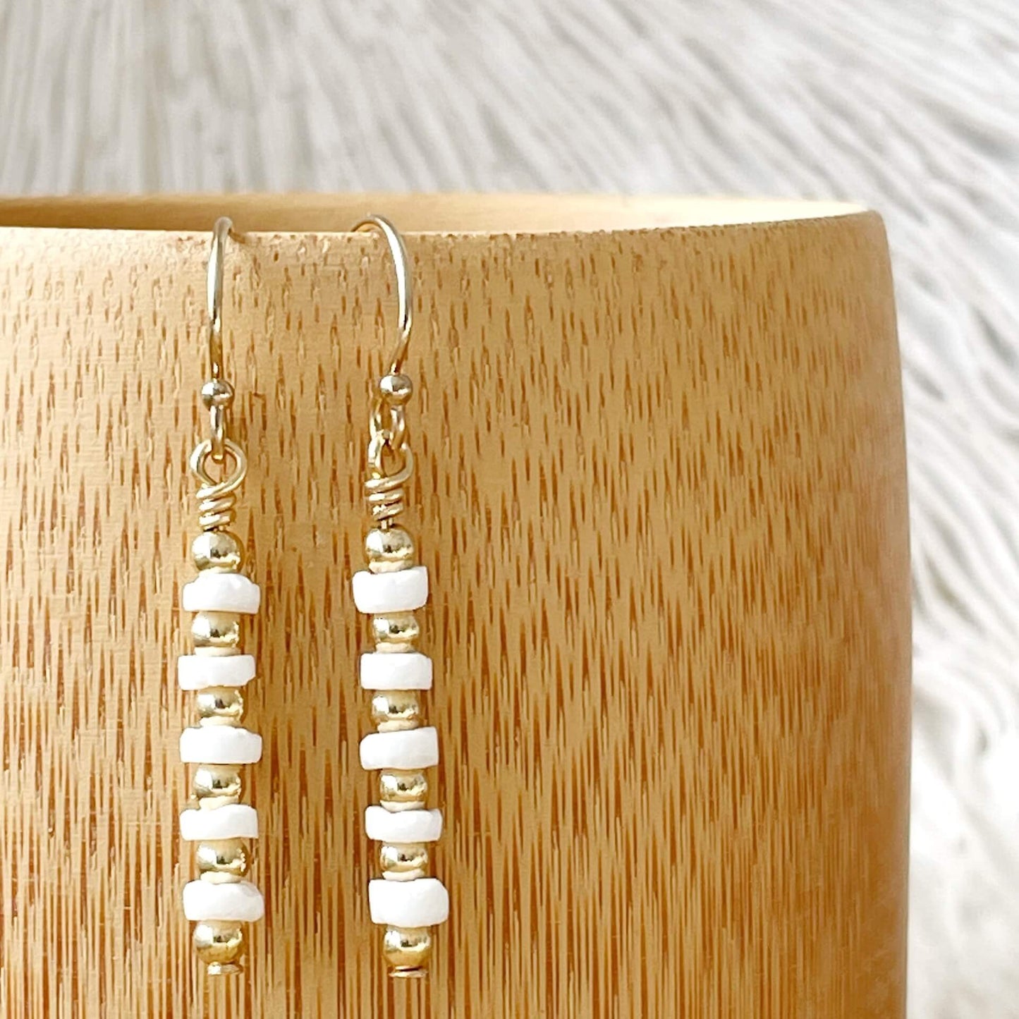 Pair of gold and white beaded earrings on a wooden stand.