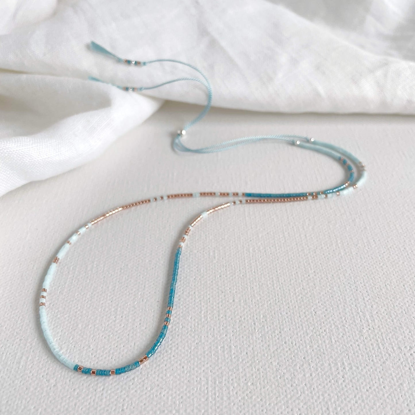 Blue and copper glass beaded necklace on pale blue silk cord with silver clasp