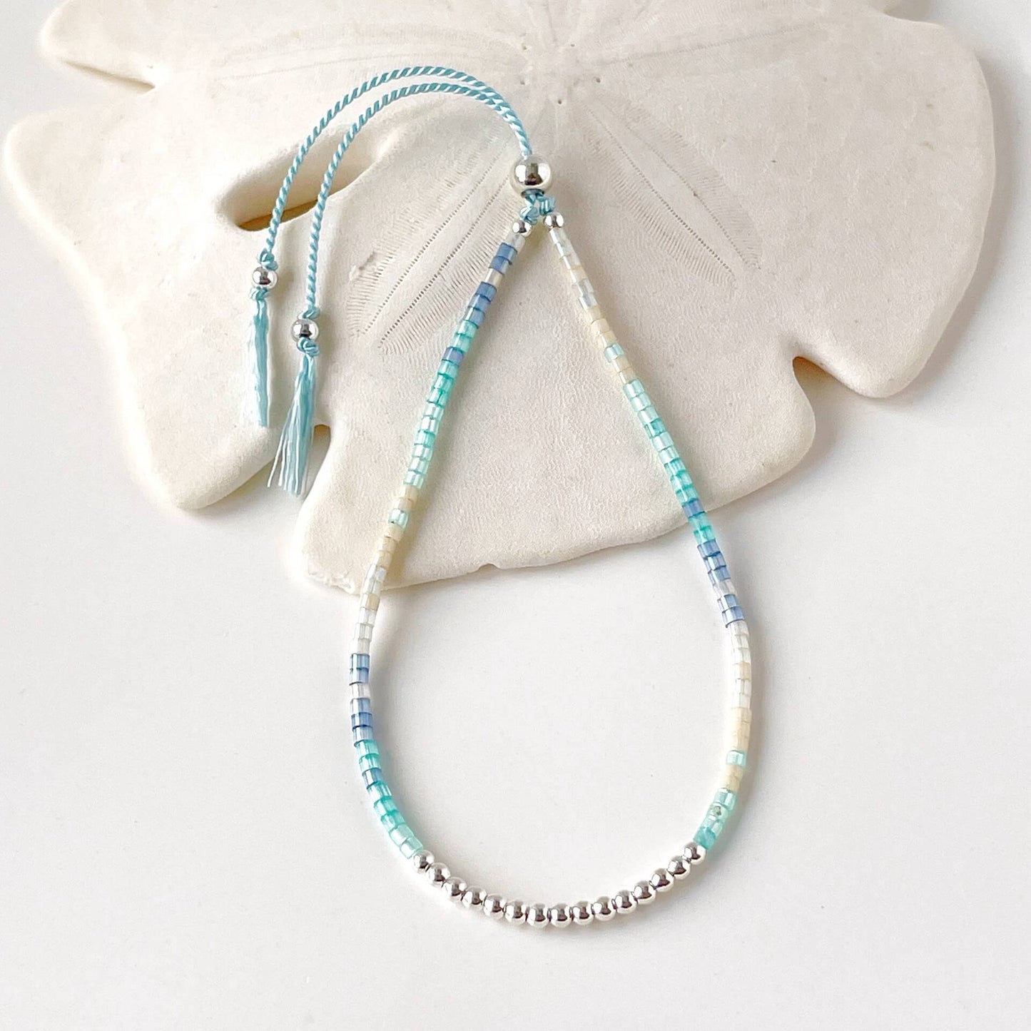 dainty beaded bracelet with blue, aqua and beige glass beads and sterling silver accents on a pale blue silk cord