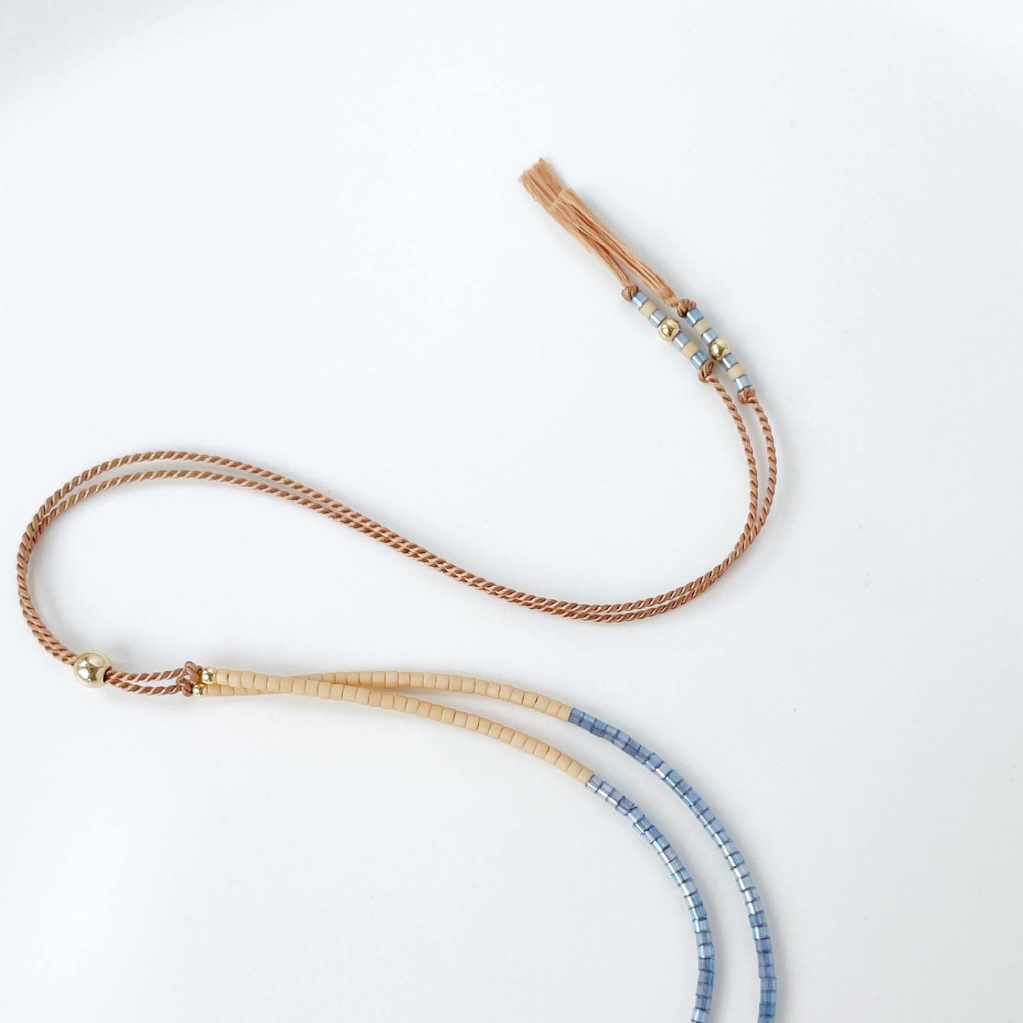 section of a blue and beige beaded necklace showing the beige silk beaded tassel ends