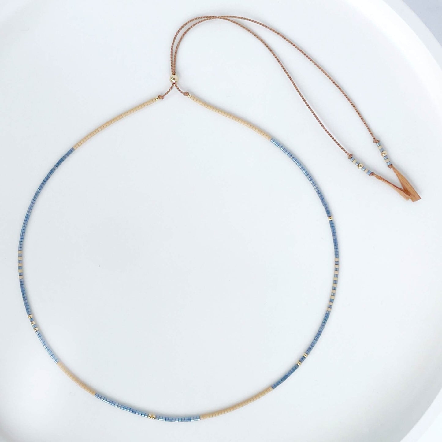 Lone Star necklace with denim blue and sandy beige Miyuki beads on beige silk cord with gold fill accents on a white background