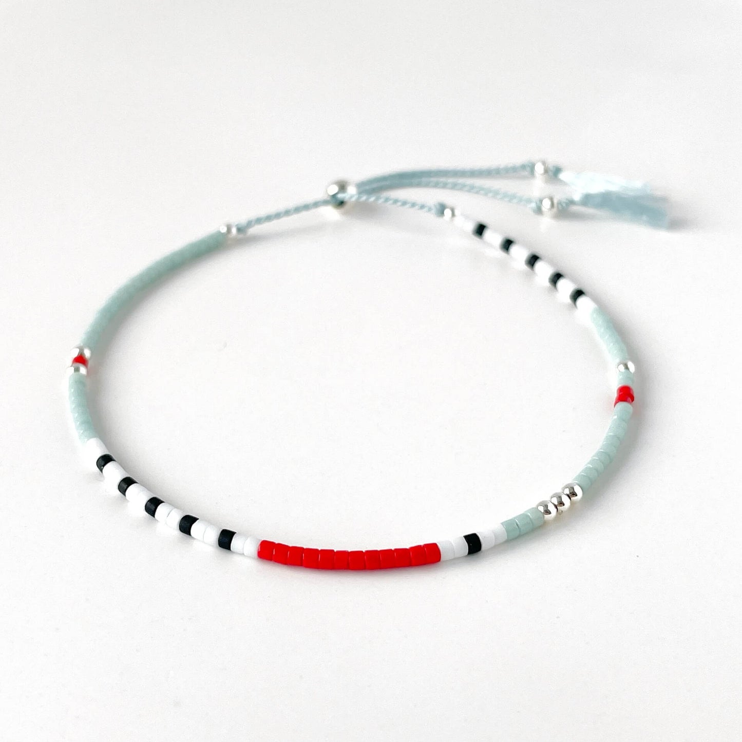 Nautical glass bead bracelet with pale blue, white, black and red beads and sterling silver accents on silk cord on a white background
