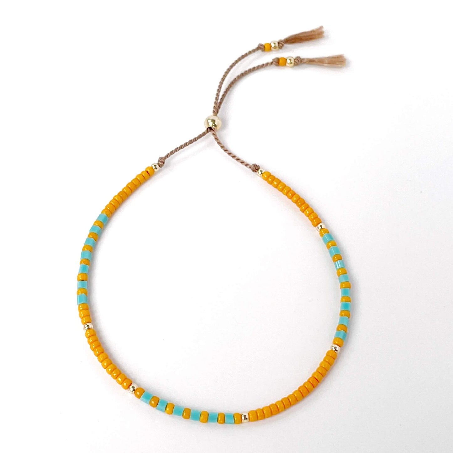 Beaded necklace with orange and blue beads on a beige silk cord with tassels and slider bead on a white background