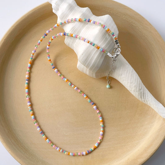 Tropical rainbow glass bead necklace with 2mm colourful beads and sterling silver lobster clasp displayed on a wooden plate