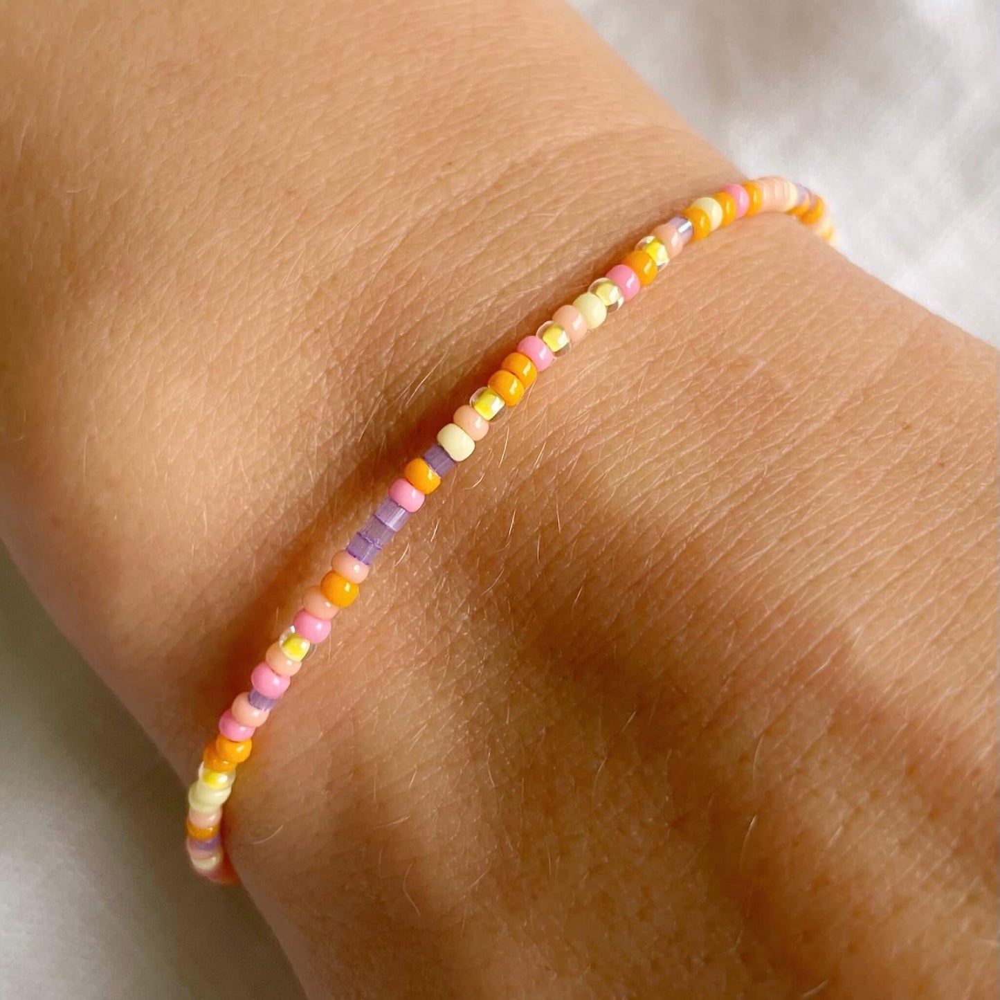 dainty beaded bracelet with tiny glass beads in yellow, orange, pink, peach and lilac worn on the wrist