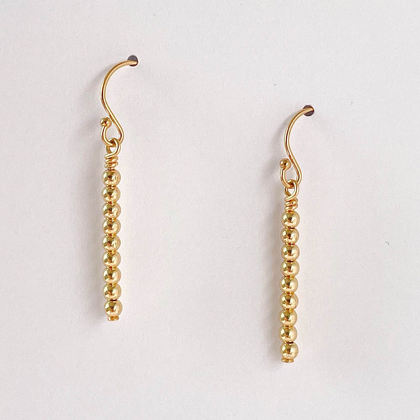 Minimalist Gold beaded dangle earrings with French ear hooks on a white background