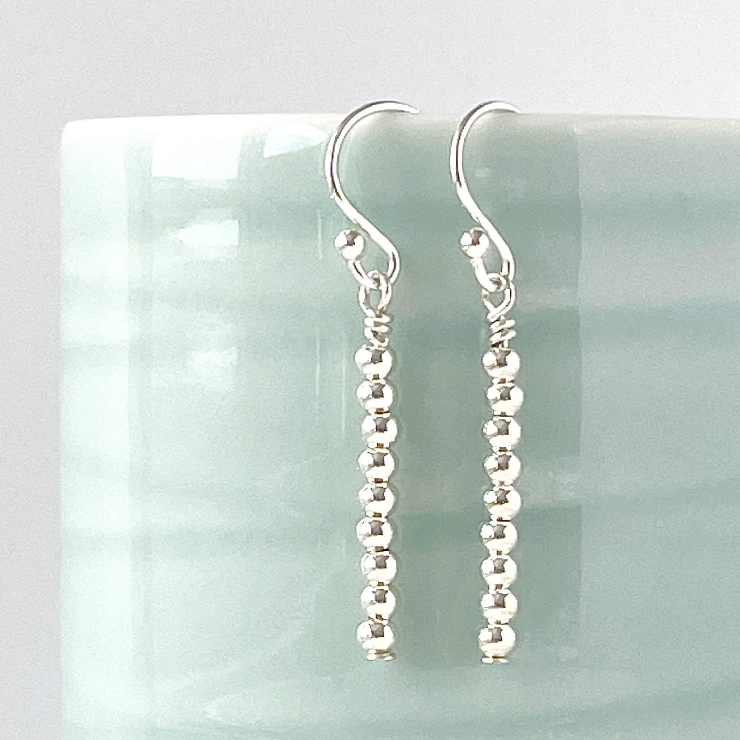 Minimalist sterling Silver beaded dangle earrings on a light aqua background