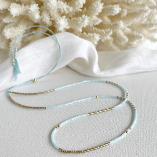 Ice Gold necklace with ice blue and gold Miyuki glass beads on pale blue silk displayed next to a piece of cora