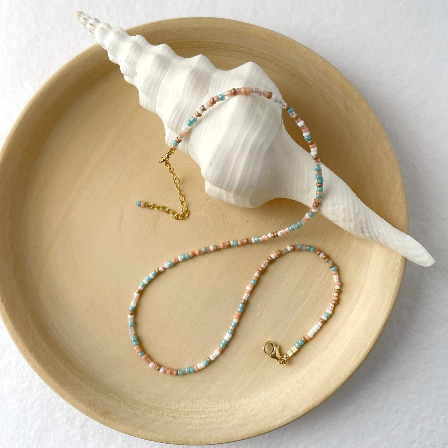 Coastal sunrise necklace with 2mm aqua, gold, peach and white glass beads and 14k gold filled accents displayed on wooden board
