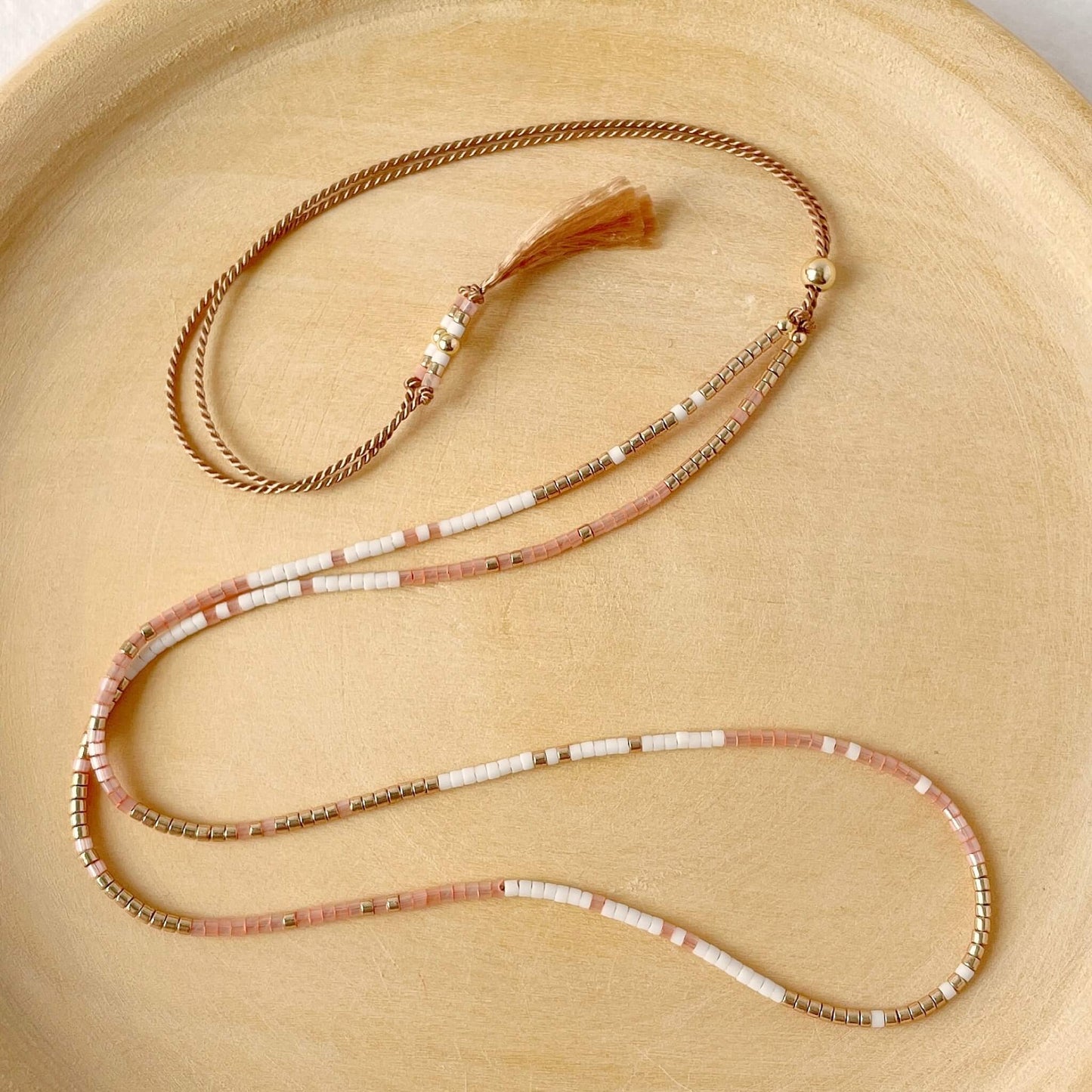 beaded necklace with peach, gold and white beads on adjustable silk cord on a wooden plate