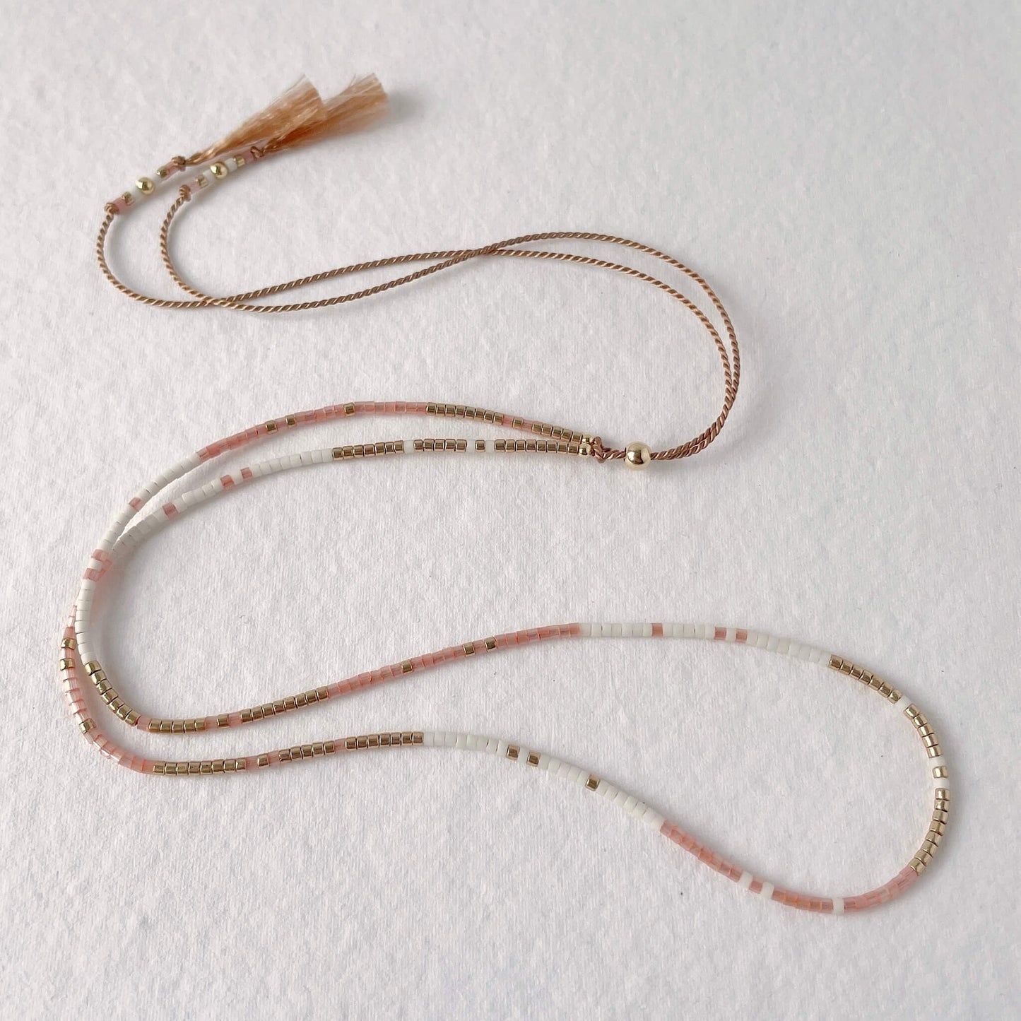 Minimal beaded necklace with peach, gold and white beads on adjustable silk cord