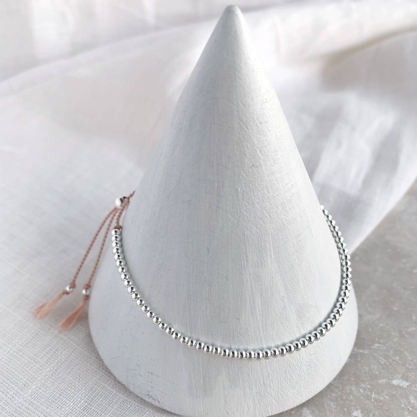 Dainty beaded bracelet on soft pink silk with 2mm sterling silver beads displayed on a cone