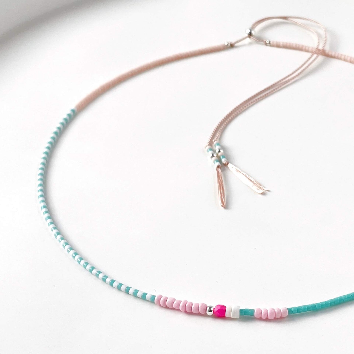 Necklace with turquoise and pink beads on a pale pink silk cord on a white background