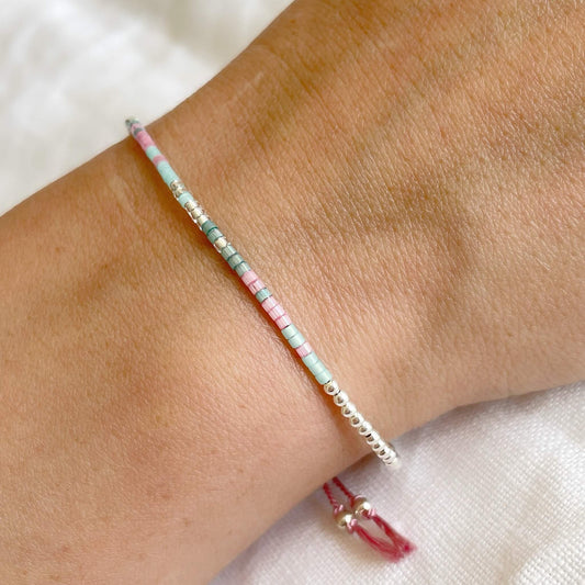 beaded silver bead bracelet with pink, green and silver glass beads on mid pink silk cord worn on a wrist