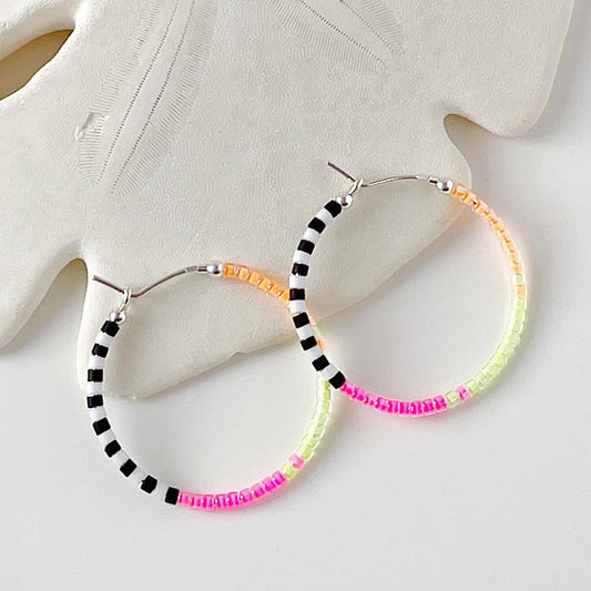 Sterling silver hoop earrings with neon pink, yellow, orange, black and white glass beads displayed lying against a white sand dollar