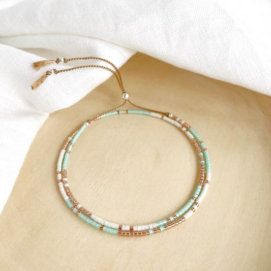 Tarifa double wrap bracelet with green aqua, white and copper glass beads with silver accents displayed against a wood background