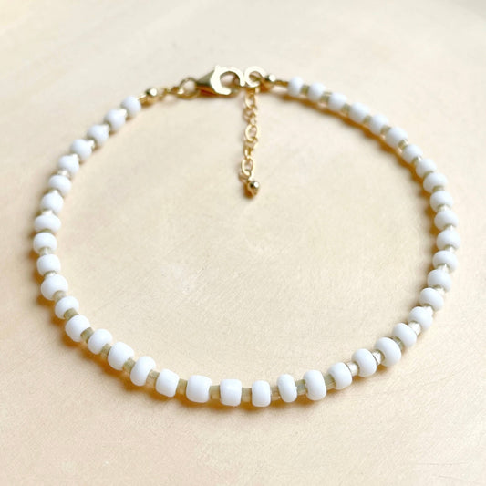 white and beige beaded anklet with gold clasp and extension chain displayed against a wooden background