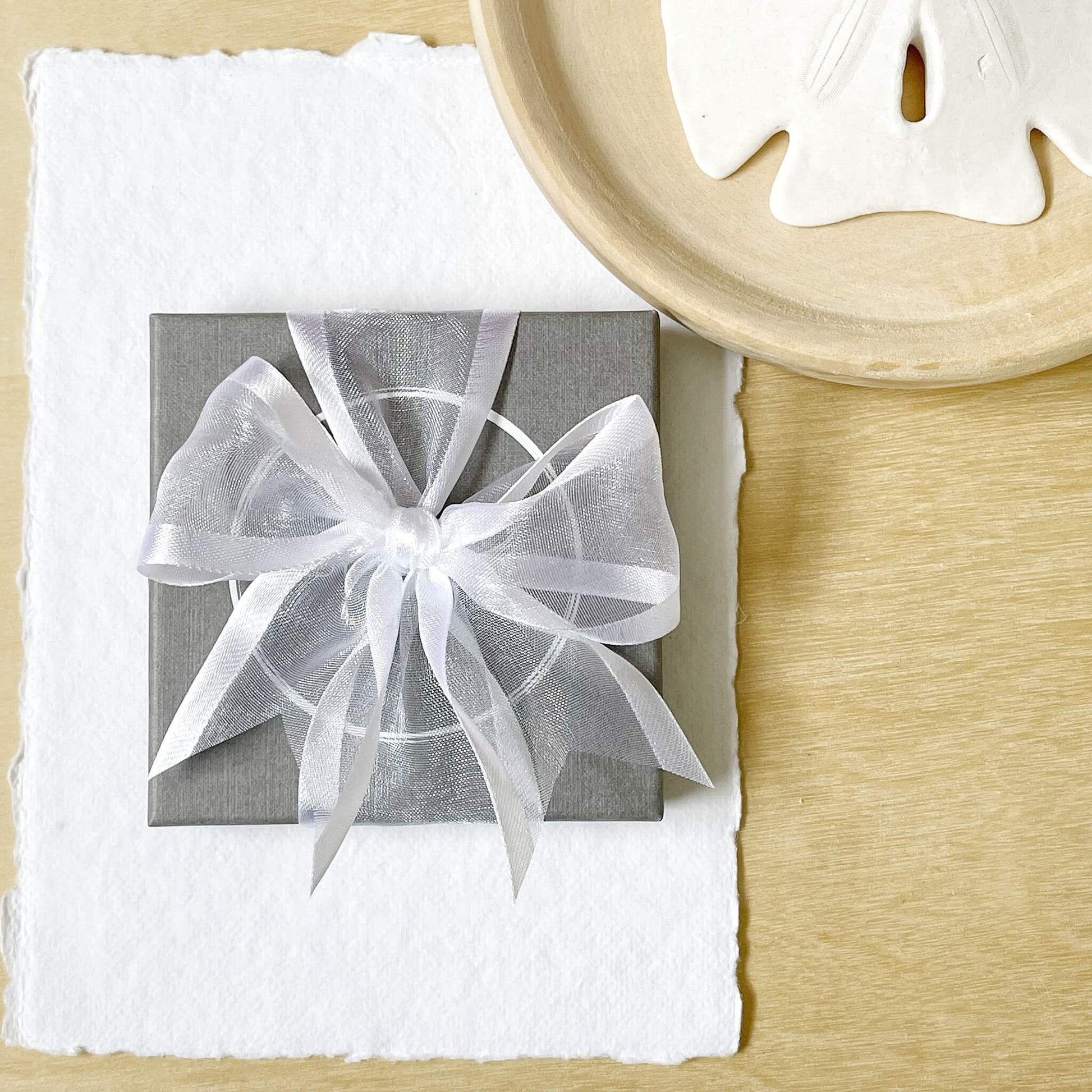 grey jewellery display gift box with white organza ribbon in a bow against a wooden background