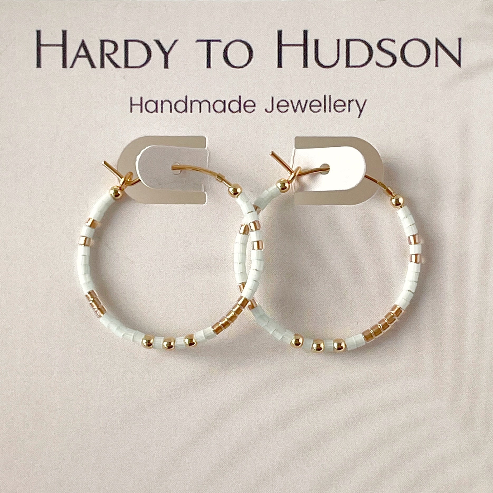 Handmade hoop earrings with pale blue and gold accents on a beige background, branded as Hardy to Hudson.
