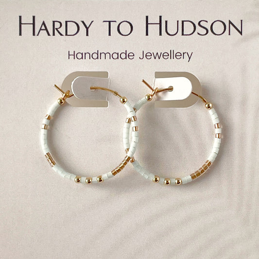 Handmade hoop earrings with pale blue and gold accents on a beige background, branded as Hardy to Hudson.
