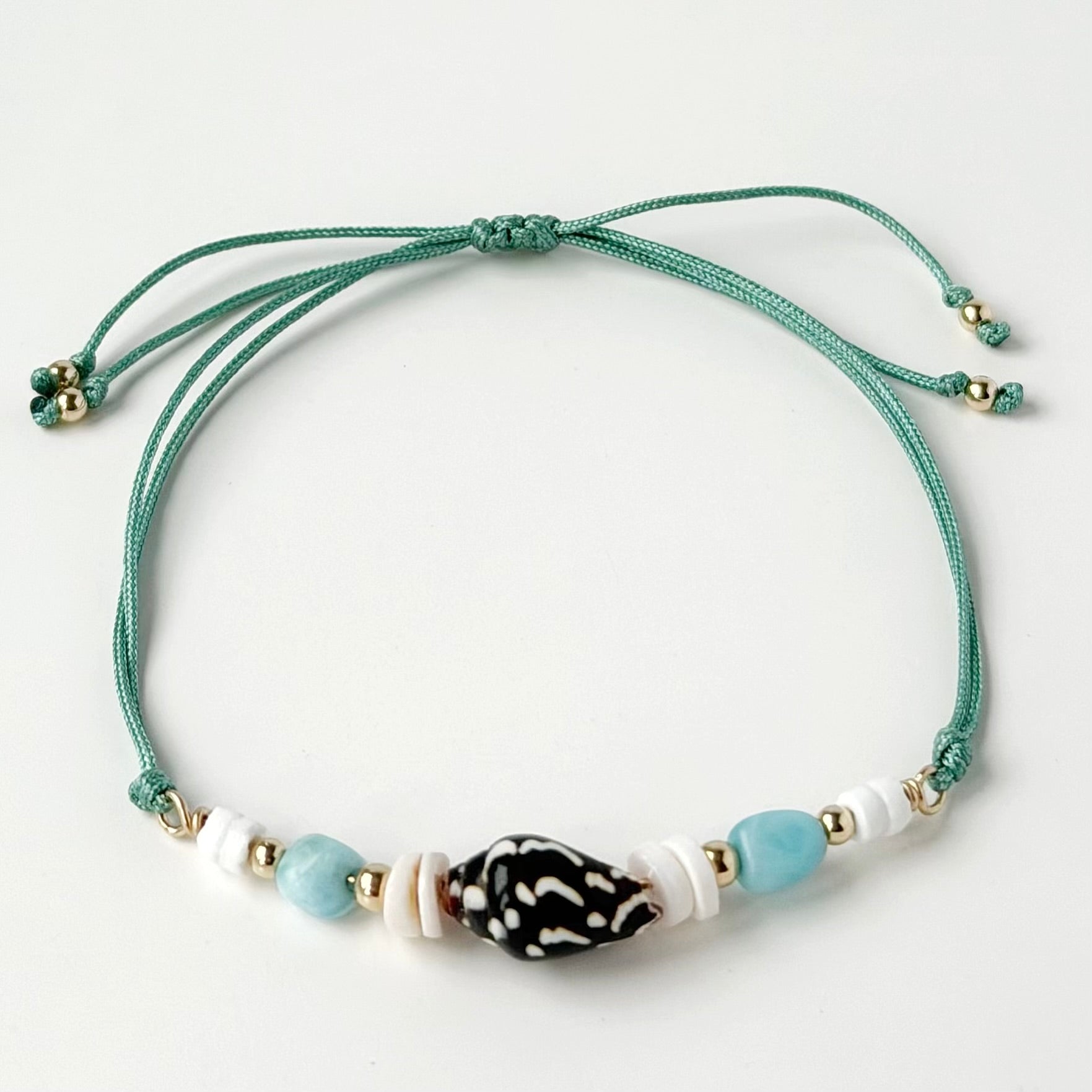 nylon teal cord bracelet with shell and gold beads on white background