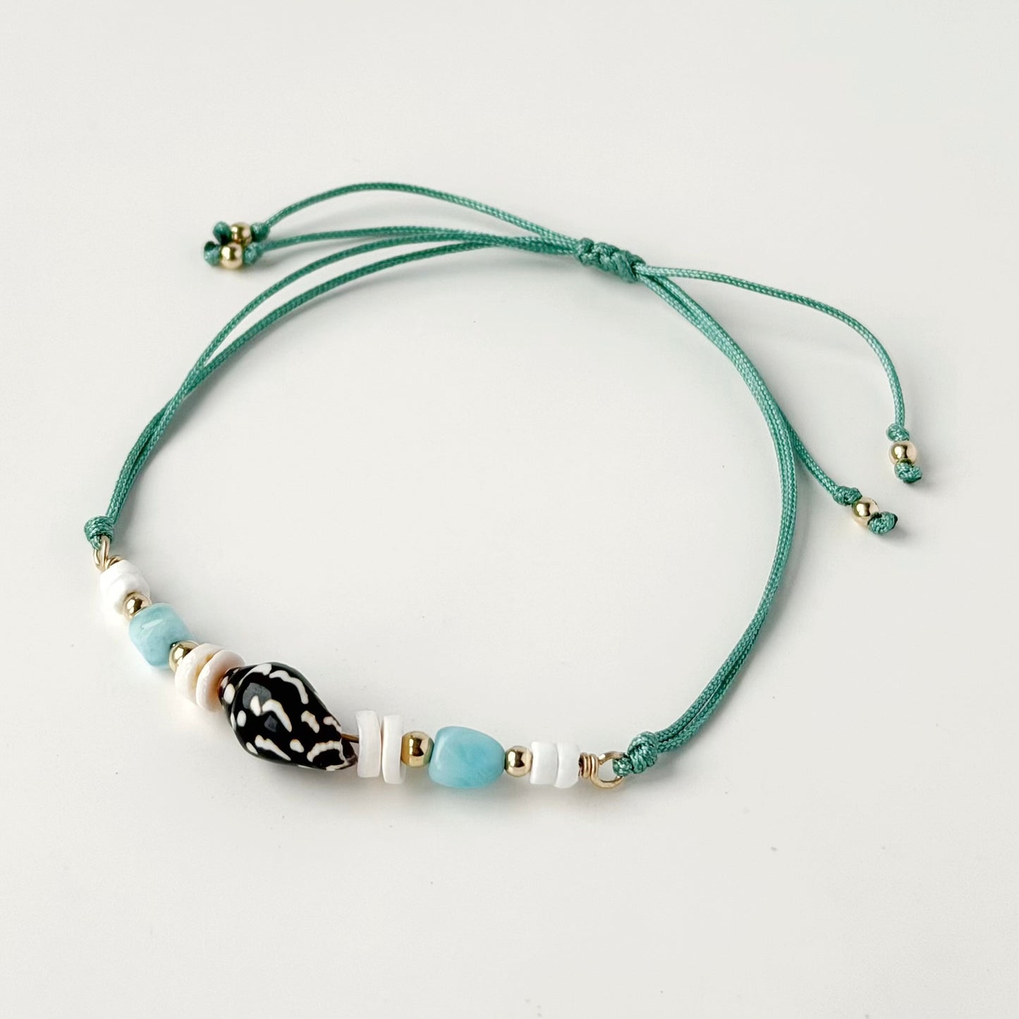 nylon teal cord bracelet with shell and gold beads on white background and tail ends