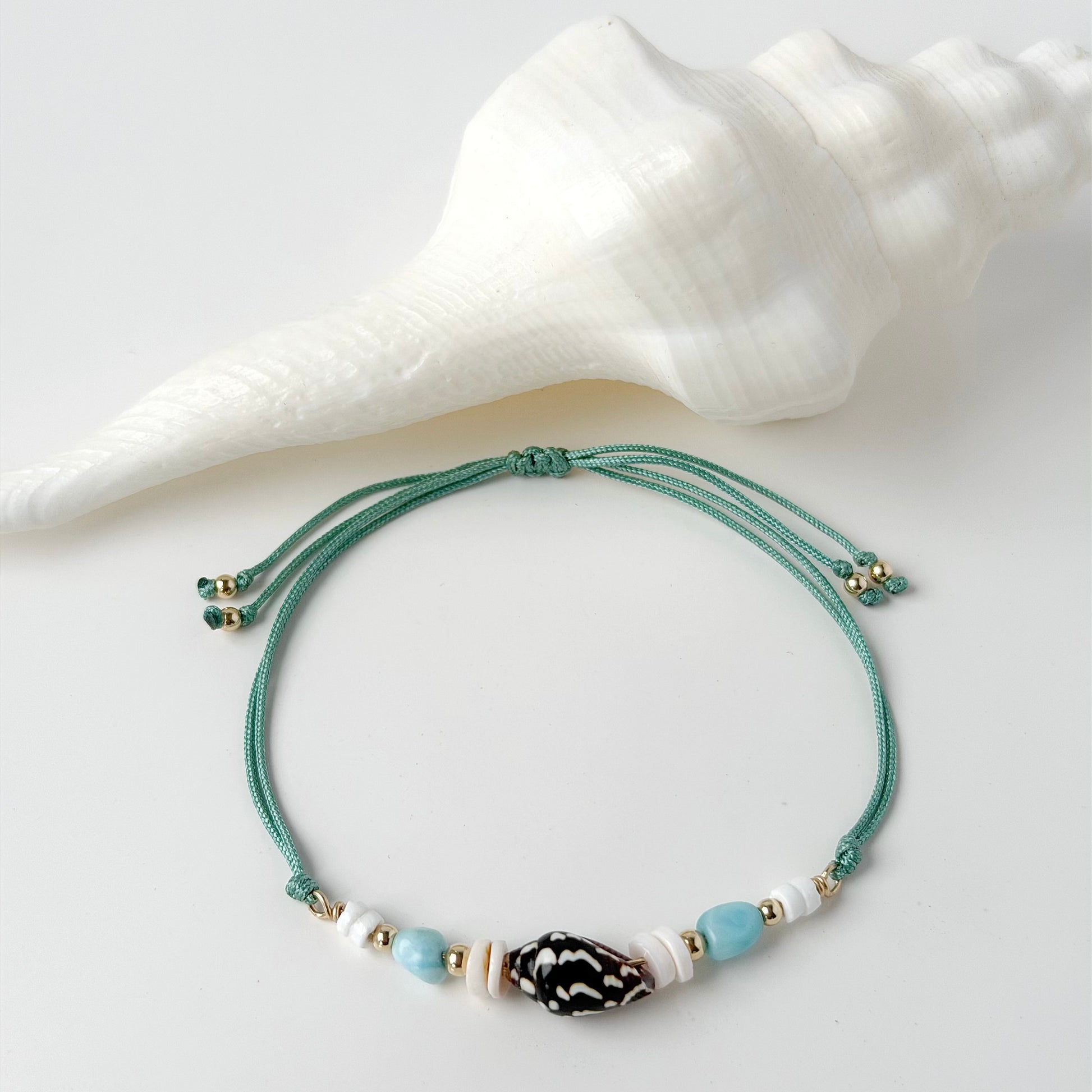 nylon teal cord bracelet with shell and gold beads on white background with white shell