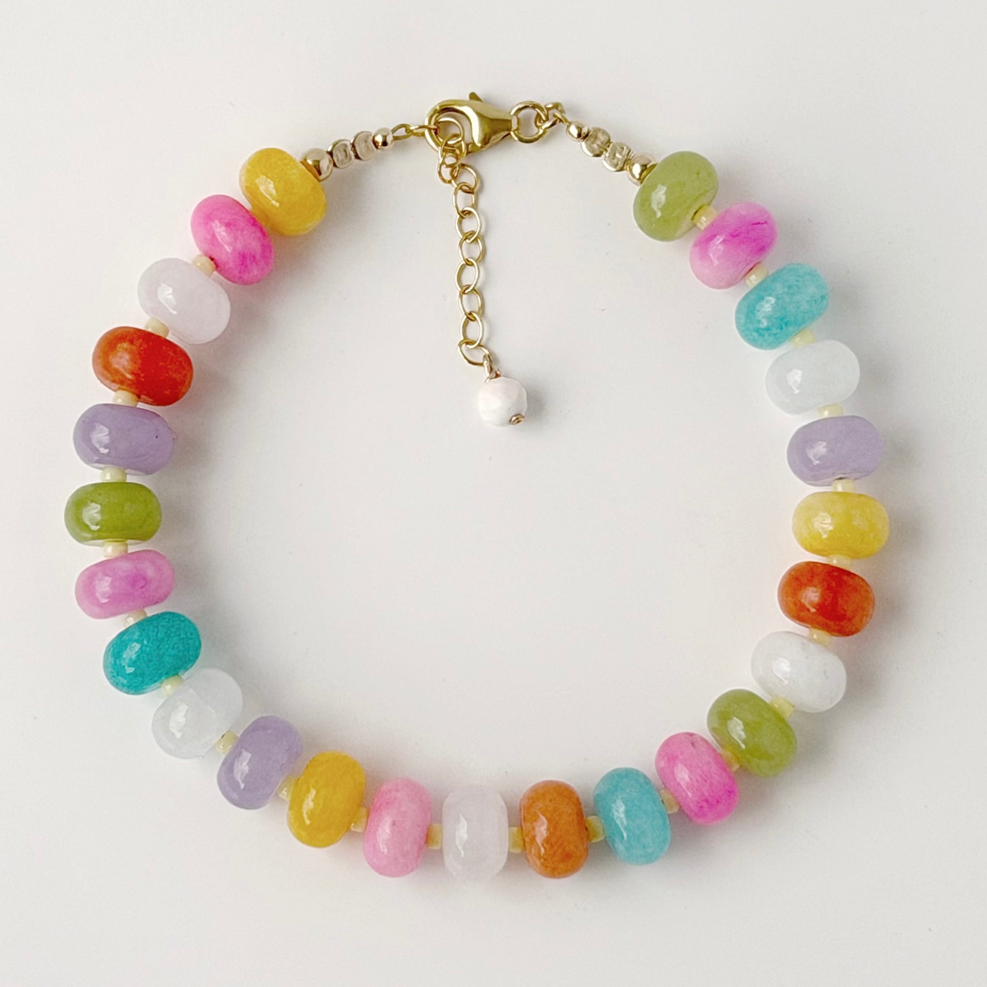 Multicolour dyed jade gemstone bead bracelet in pink blue turquoise apricot and green with gold fill clasp on a neutral surface
