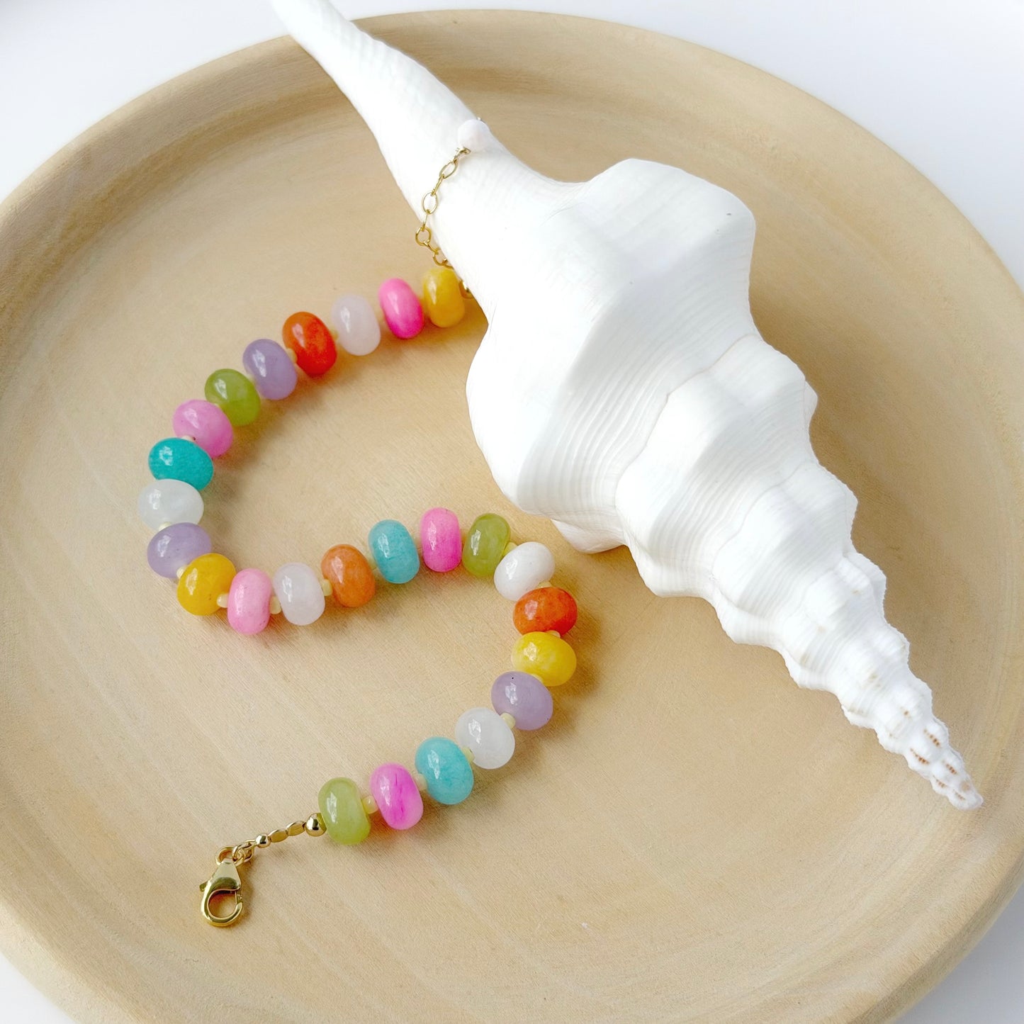 Colorful beaded bracelet on a wooden surface with a large shell.