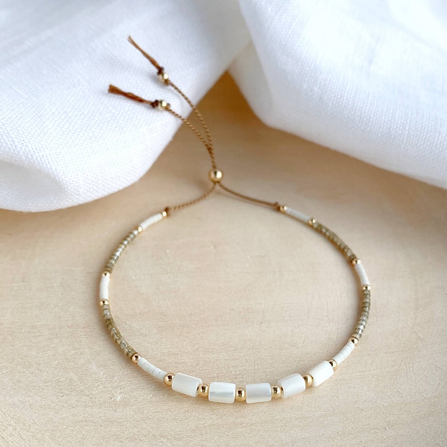 Dainty beaded bracelet with beige and white glass beads, mother of pearl, and 14k gold fill on adjustable silk cord