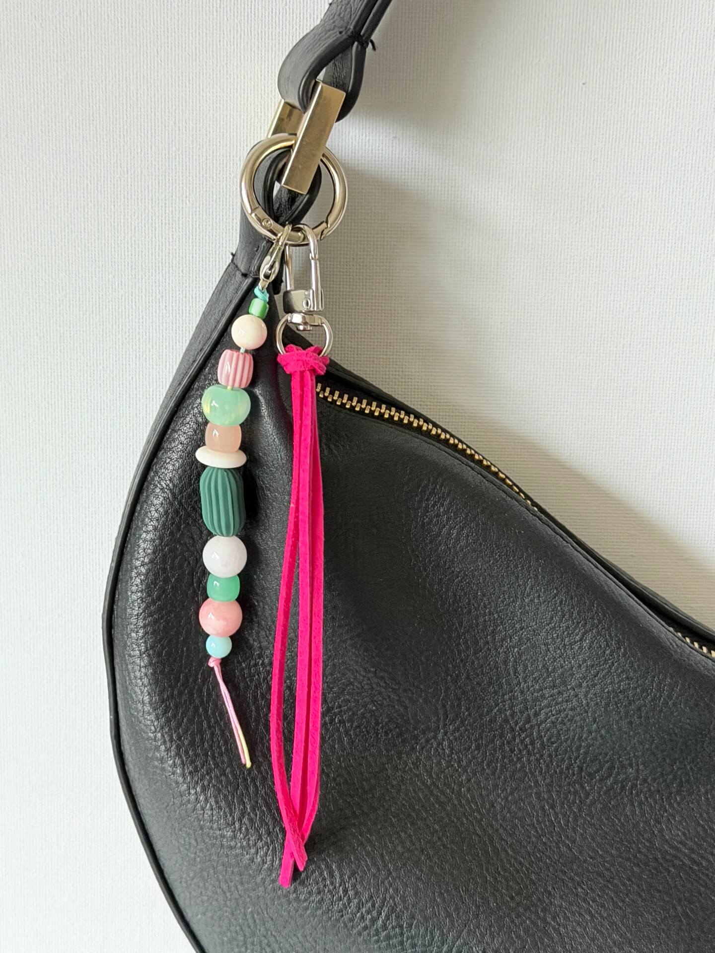 beaded bag charm with neon pink suedette tassel and chunky pink, green and white bead displayed on a black bag