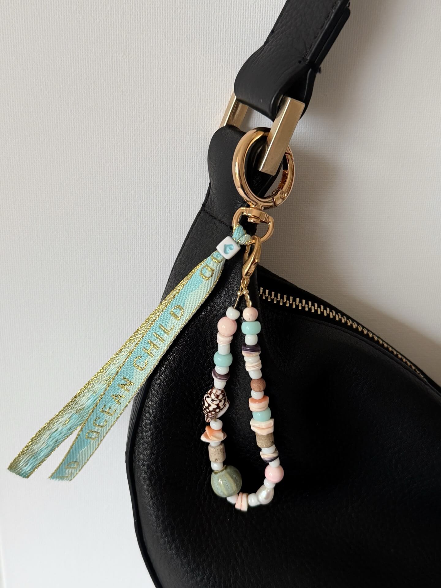 bag charm with shell, glass, and wood beads with a blue and gold embroidered ocean child ribbon tassel attached to a black bag