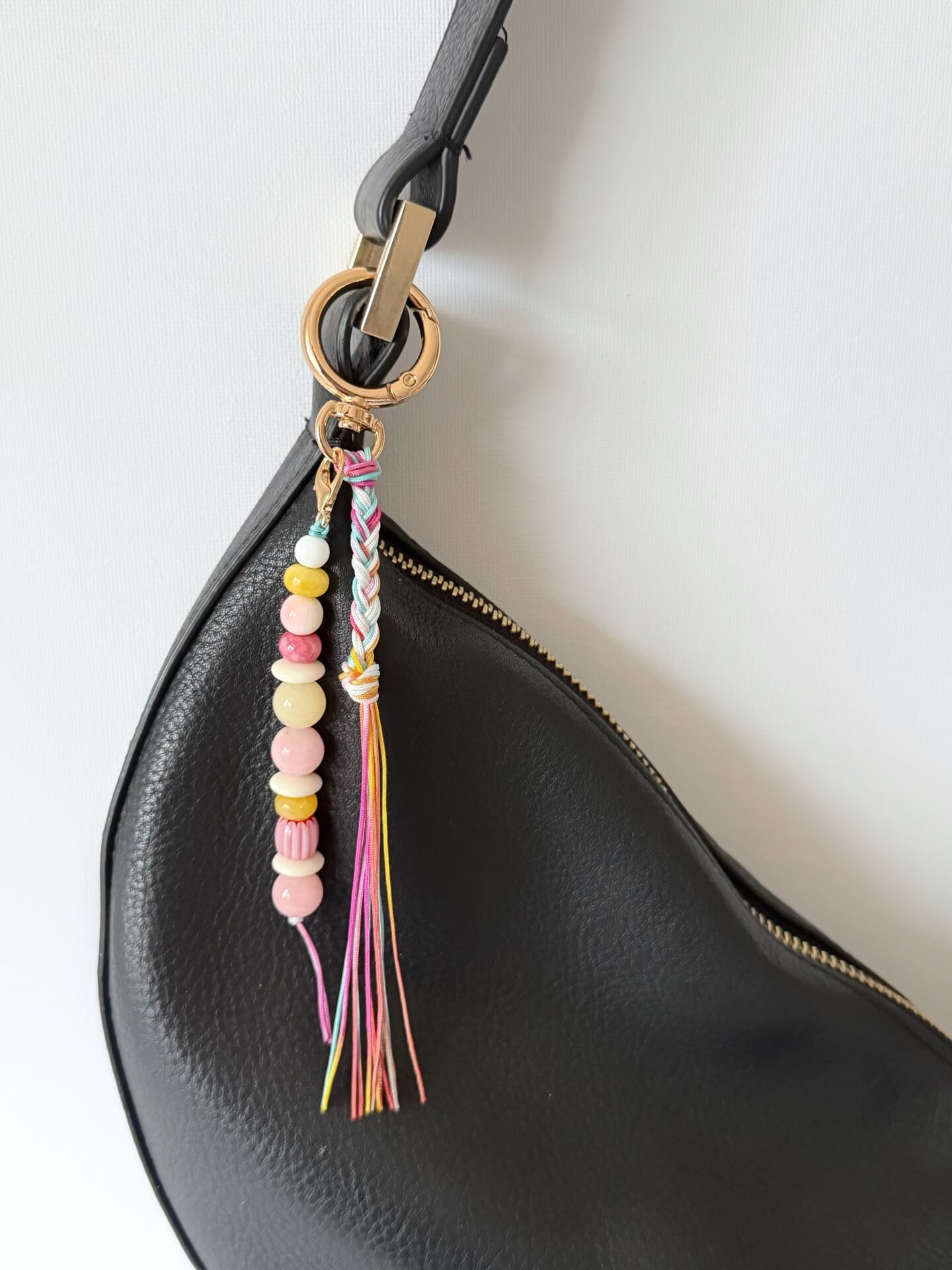 beaded bag charm with red, yellow, white and pink beads with a rainbow coloured nylon braided tassel displayed on a black bag