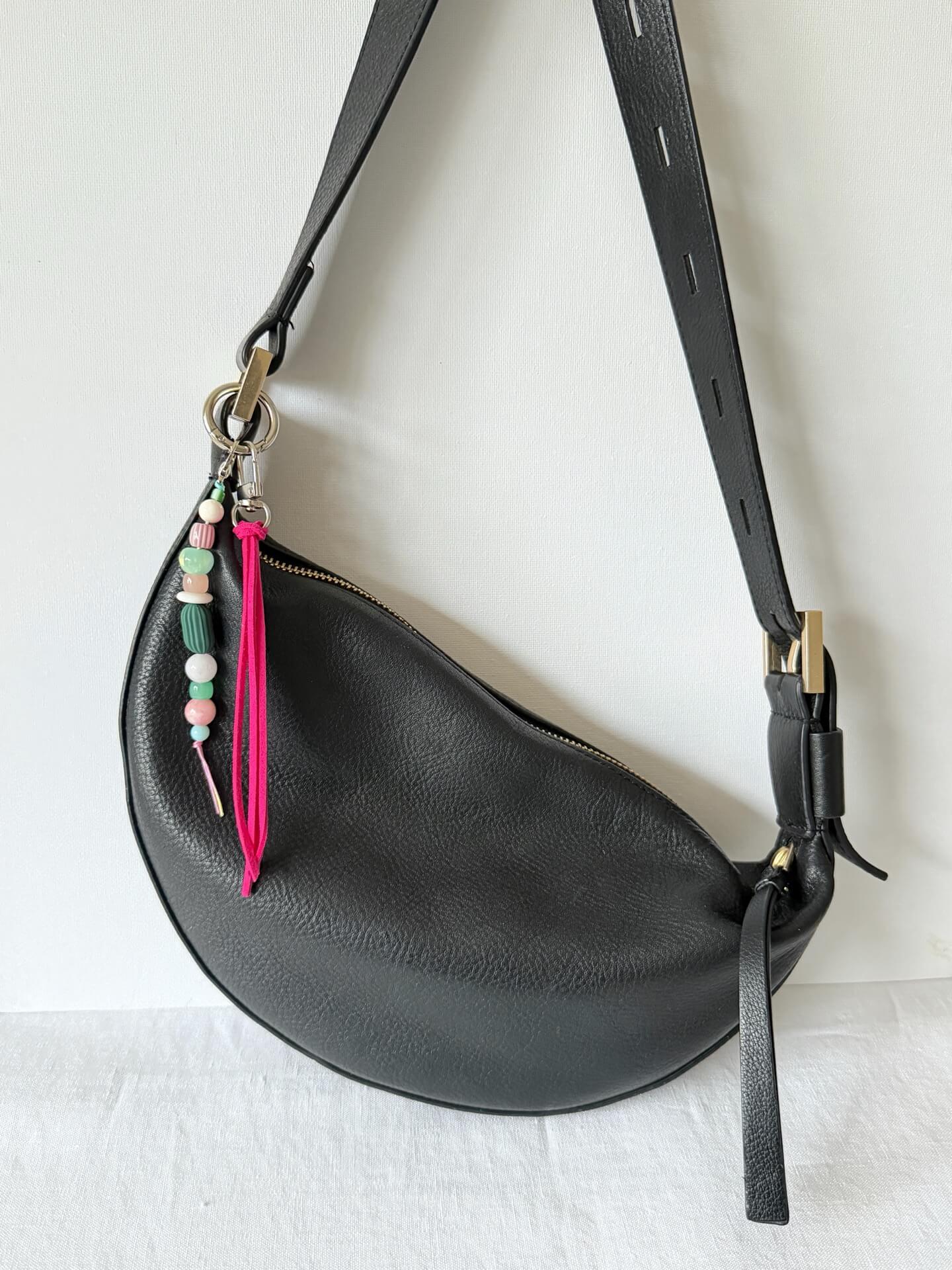 beaded bag charm with neon pink suedette tassel and chunky pink, green and white bead attached to a black bag